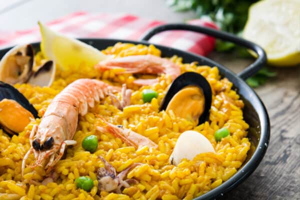 Magefesa black enameled steel paella pan with rice, shrimps and lemon over a wooden table