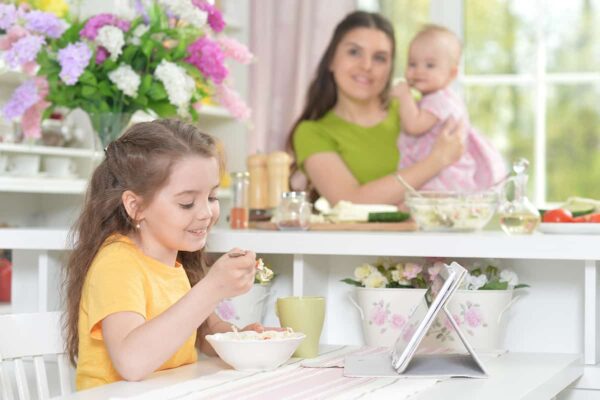 red cute little girl eating fresh salad at kitchen table -