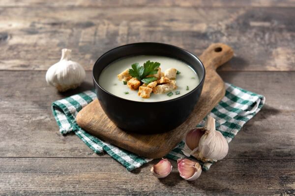 red garlic soup topped with croutons in black bowl on wooden table -